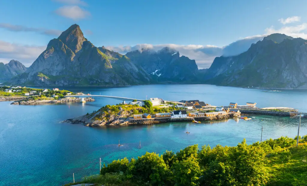 Breathtaking summer view of Lofoten Islands featuring the scenic beauty of mountains, a tranquil sea, and a quaint village in Norway, perfect for adventure and serene getaways.