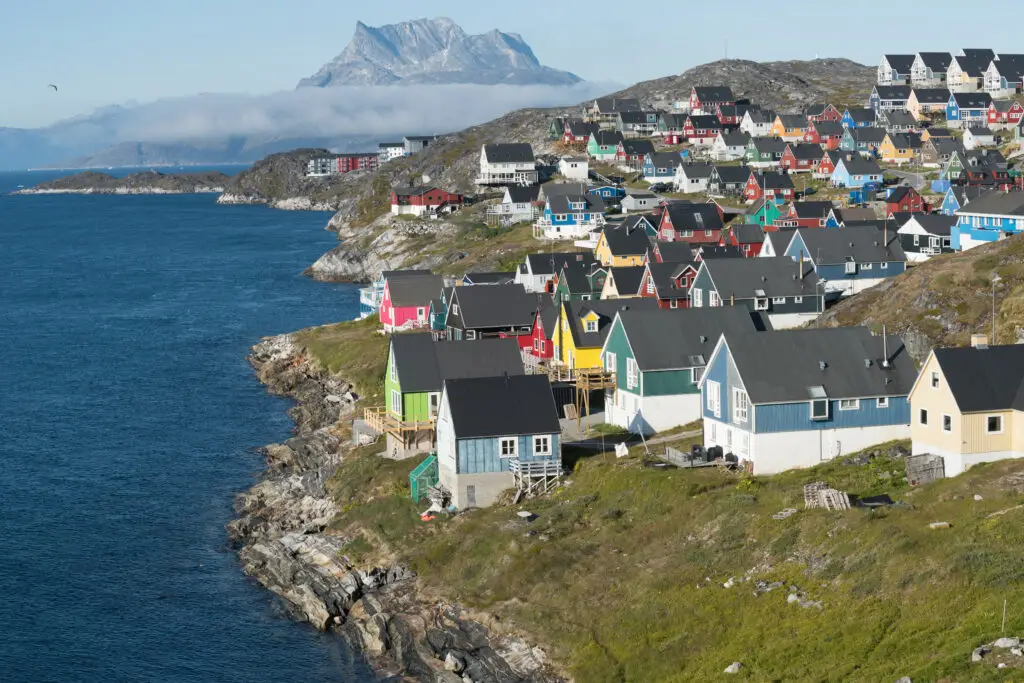 Colorful houses in Nuuk, Greenland, with a mountain backdrop under a clear blue sky, showcasing the charming capital's unique architecture and scenic coastal location.