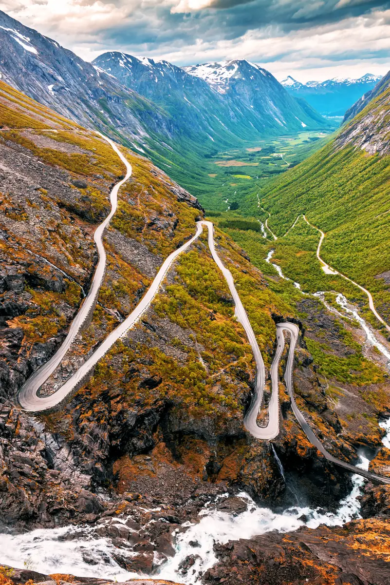 Scenic view of the winding Trollstigen road amidst lush green landscapes and mountain peaks in Norway, highlighting dramatic curves and rugged terrain for adventurous travelers.