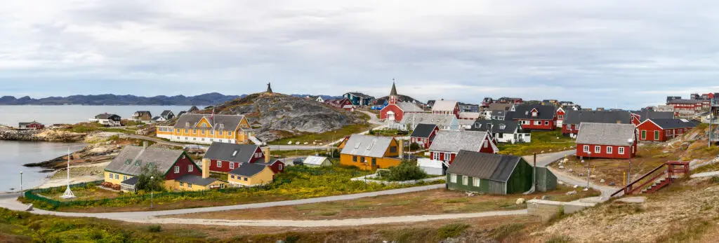 Panoramic view of colorful houses in Nuuk, Greenland featuring Det gamle Sygehus school, the cathedral, and Hans Egede statue, highlighting iconic tourist attractions and cultural heritage.
