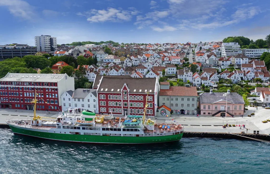 Panoramic view of Stavanger, Norway, featuring a vintage green and white ship docked near colorful traditional Scandinavian buildings.