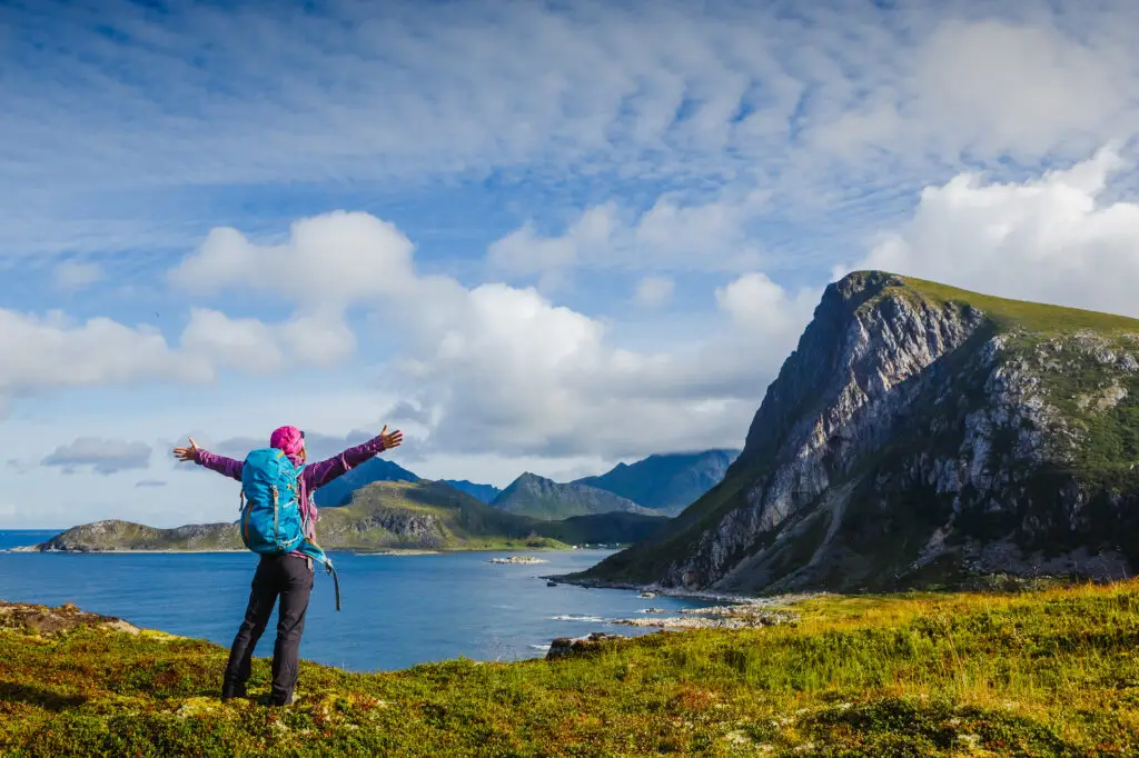 Woman hiker with arms spread wide standing on a mountain top overlooking a scenic Norwegian fjord in Lofotens, symbolizing travel, adventure, and a healthy lifestyle