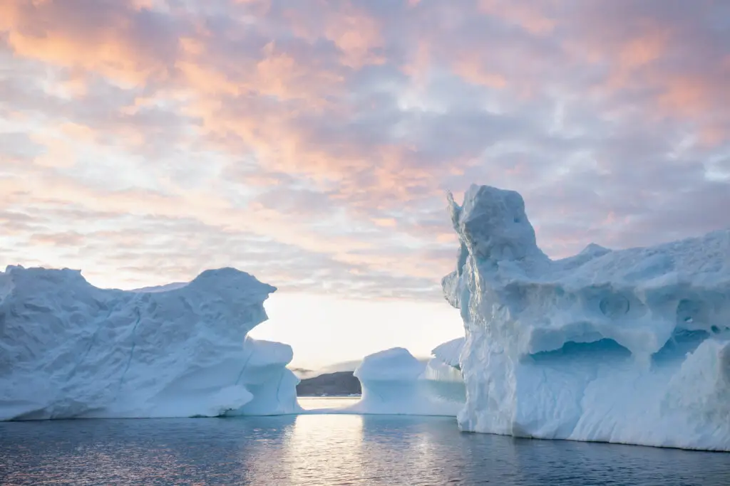 Arctic sunrise in Greenland icefjord with monumental icebergs and colorful morning sky, illustrating climate change and natural beauty in Scandinavia.