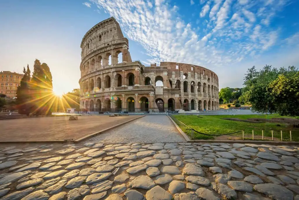 Sunrise at the Colosseum in Rome, Italy, showcasing the ancient amphitheatre's iconic arches and the original Roman cobblestone road in the foreground.
