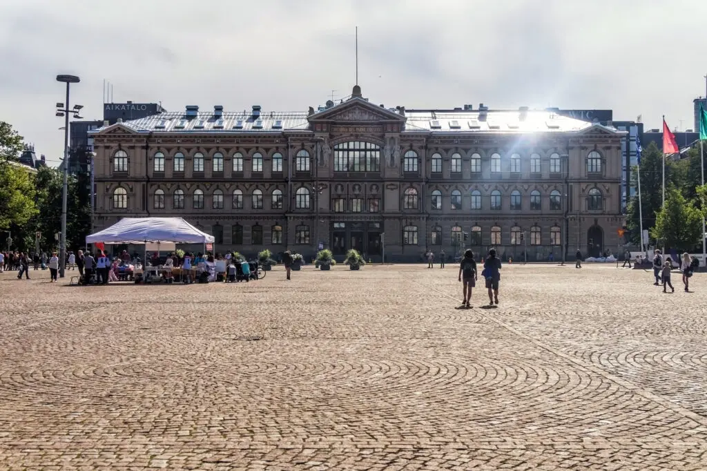 View of Ateneum Art Museum in Helsinki, Finland, showcasing its grand architecture with tourists on the cobblestone Rautatientori, Railway Square, on a sunny day.