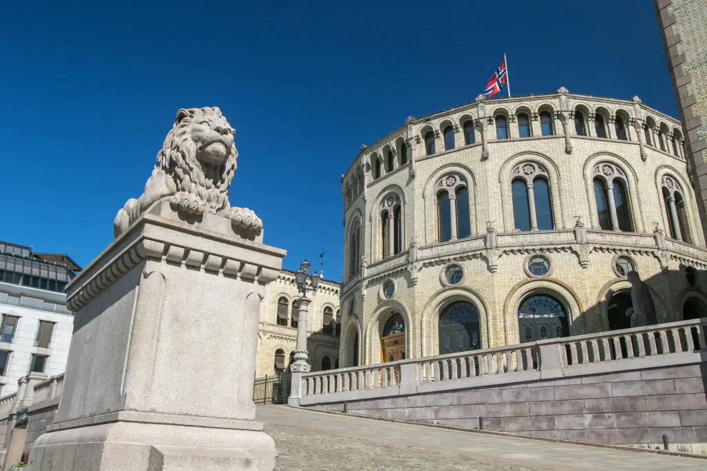 Stone lion statue in front of the Norwegian Parliament building, Stortinget, under a clear blue sky in Oslo, Norway.