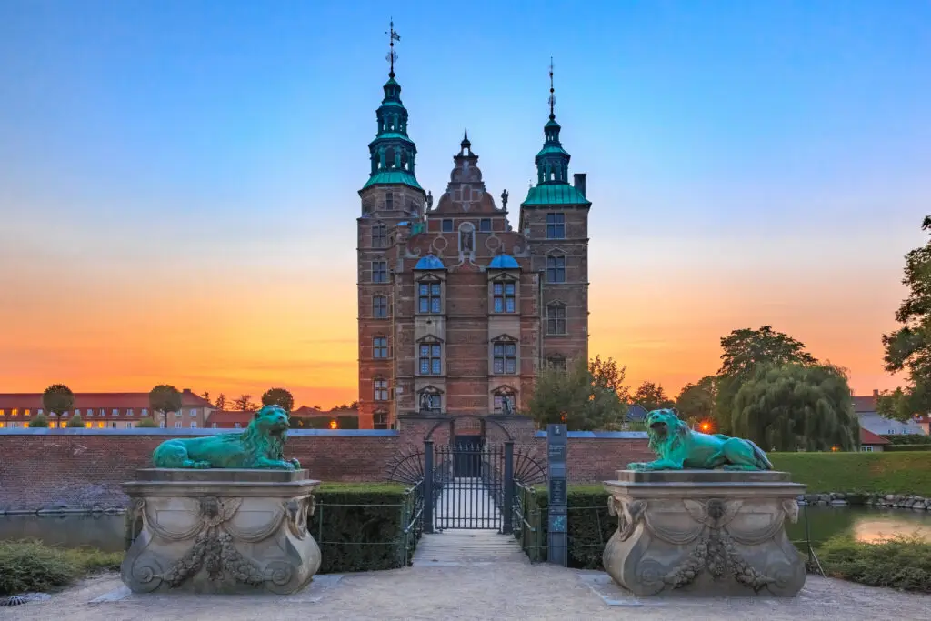 Sunset view of Rosenborg Castle in Copenhagen, Denmark, featuring ornate gates and lion sculptures.