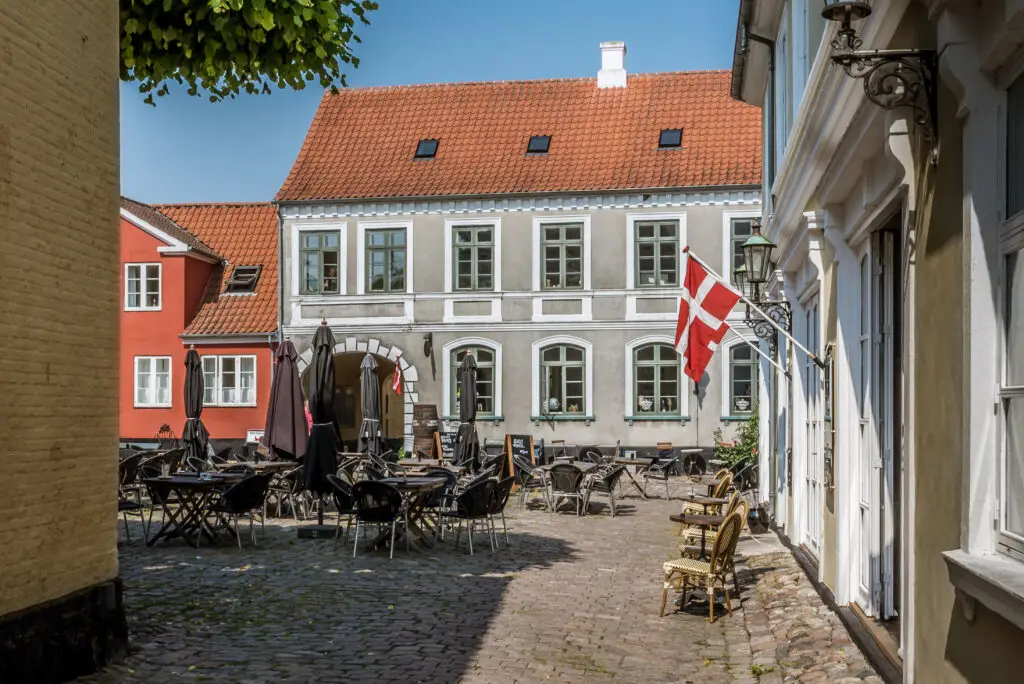 Danish flag waving over a charming outdoor café in the cobblestoned square of Aeroskobing, Denmark, showcasing traditional architecture and a serene atmosphere.
