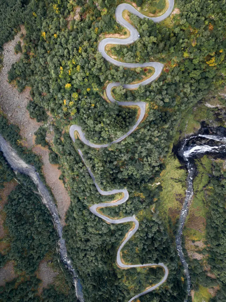 Aerial view of the serpentine road Stalheimskleiva in Norway, surrounded by dense green forests and a flowing river.