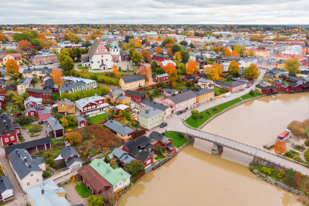 Aerial view of Porvoo Old Town in autumn showing the colorful foliage, historic wooden buildings, and the Porvoonjoki River, with the Porvoo Cathedral prominent in Finland.