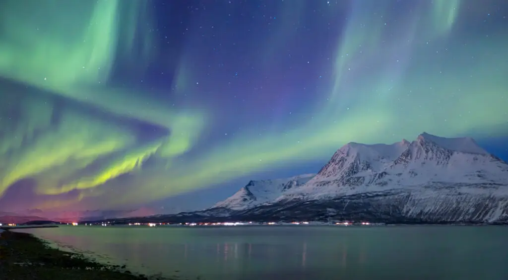 Stunning view of the Northern Lights over snow-covered mountains in Tromso, Norway, reflecting in the calm waters below
