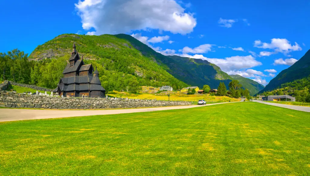 Borgund Stave Church in Norway, an ancient wooden church amidst lush green landscape under blue skies, perfect for Scandinavian heritage tours