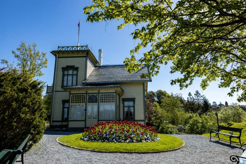 Edvard Grieg's home in Norway, featuring a picturesque garden with vibrant tulips and a classical wooden bench, under clear blue skies.