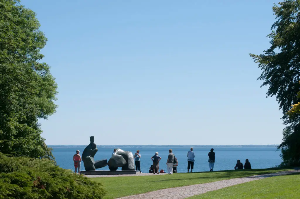 Visitors enjoying the outdoor sculpture park at the Louisiana Museum of Modern Art in Denmark, showcasing modernist art and architecture with a picturesque coastal backdrop.