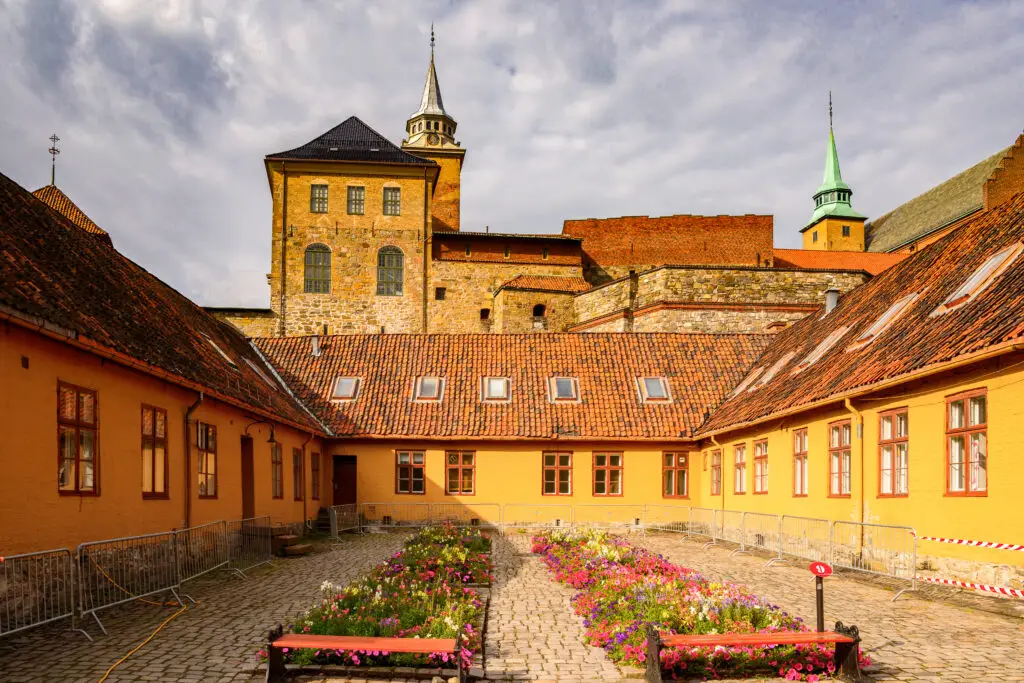 Sunny day at Akershus Fortress in Oslo, Norway showing the medieval stone architecture and a colorful courtyard with flowers.
