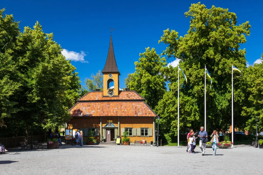 Visitors exploring the historic town square with an old church in Sigtuna, Sweden, on a sunny day.