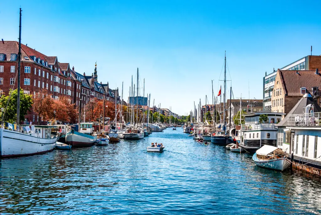 Sunny view of Christianshavn harbor in Copenhagen, Denmark, with colorful boats and historic red brick buildings along the waterfront
