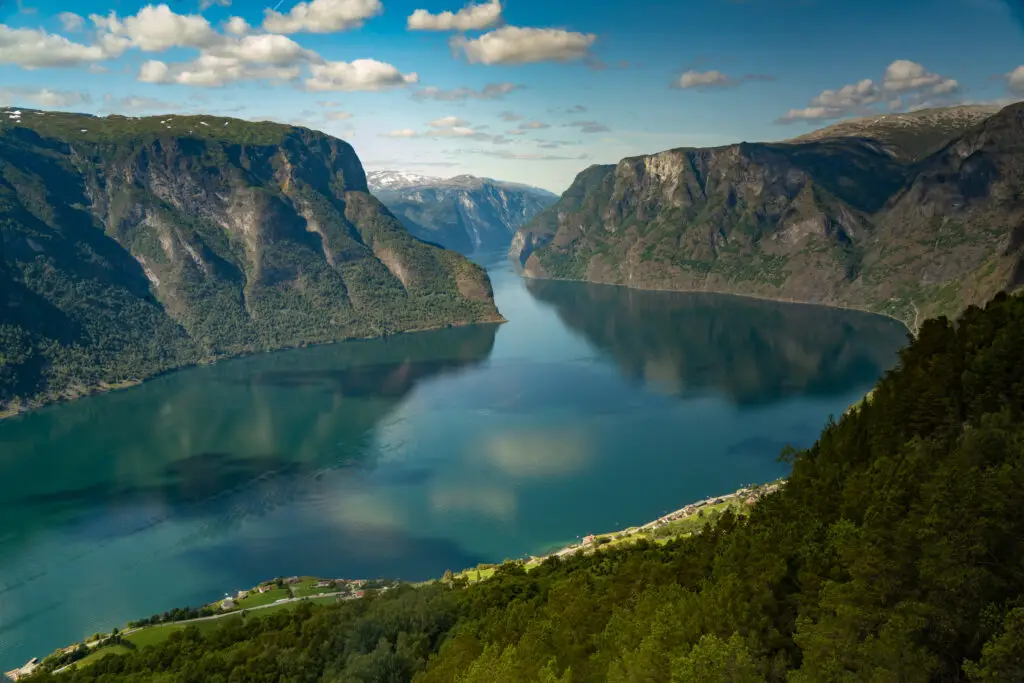 Panoramic view of Aurlandsfjord from Stegastein viewpoint, showcasing the serene waters and dramatic green cliffs under a bright sky, in Vestland, Norway.