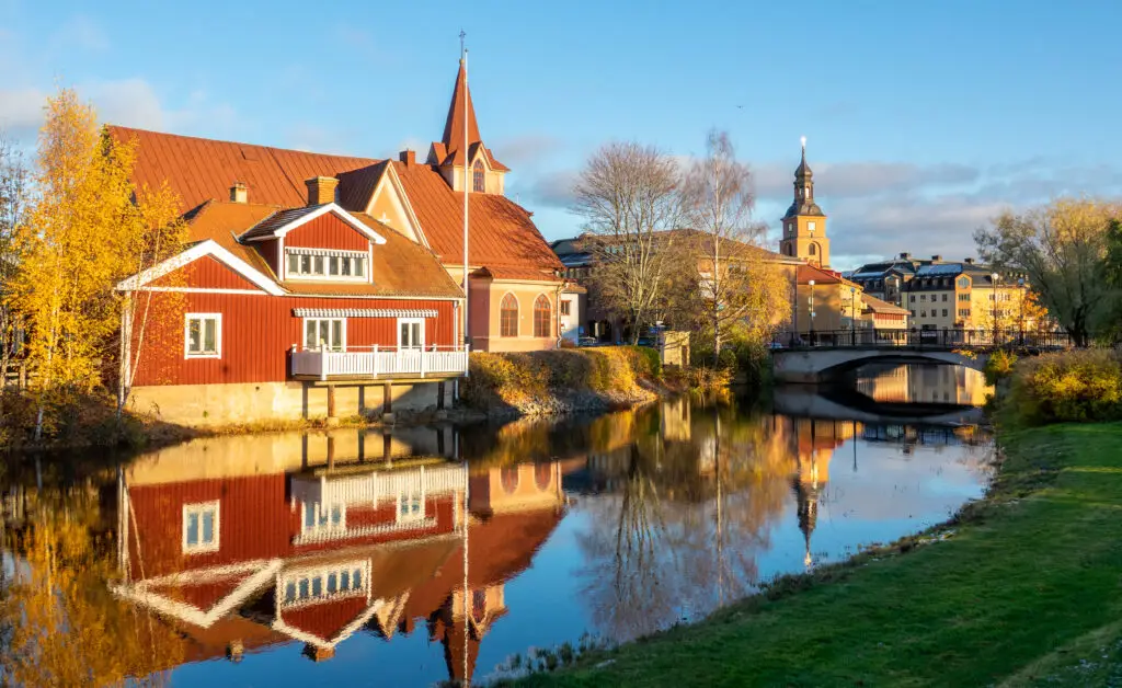 Traditional red wooden houses reflecting in the river at the picturesque old town of Falun, Dalarna, Sweden, showcasing Scandinavian cultural architecture.