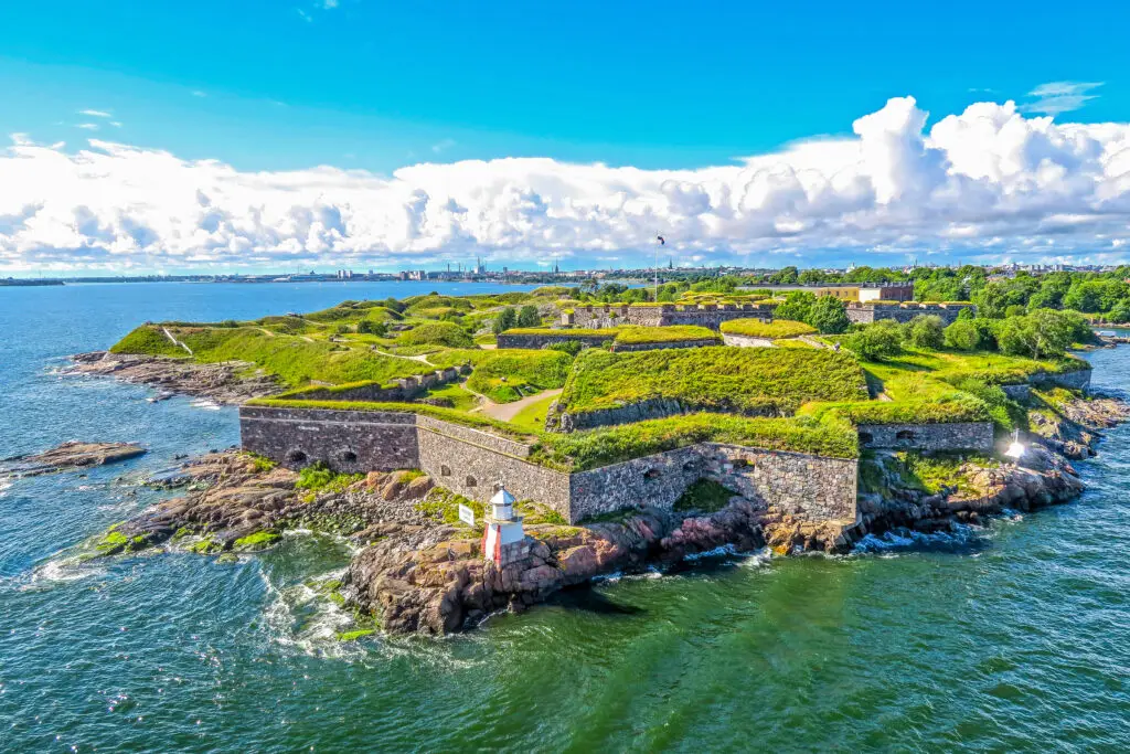Aerial view of Suomenlinna fortress in Helsinki, Finland featuring historic walls and green grounds on a sunny day with city skyline in the background