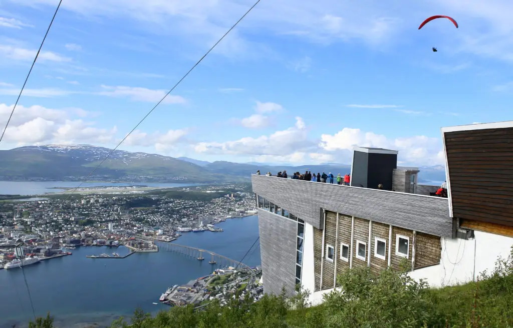Panoramic view of Tromso city from Mt. Storsteinen overlooking the fjord, cable car lines, and a paraglider in summer, Tromso, Norway.