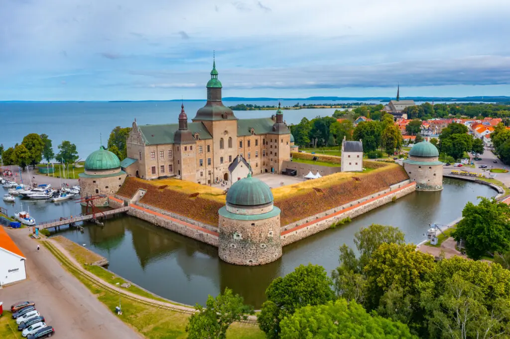 Aerial view of the historic Vadstena Castle in Sweden, surrounded by water and lush greenery, showcasing its impressive architecture and scenic location for tourists.