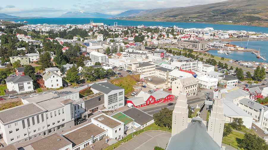 Aerial view of Akureyri Town in Iceland showcasing the dense building landscape, vibrant red bridge, bustling port area, and surrounding mountains for scenic tours.
