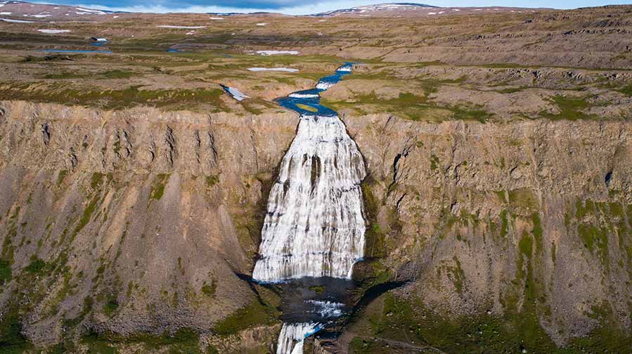 Aerial view of Dynjandi, an iconic multi-tiered waterfall in Iceland, showcasing dramatic cascades down rugged cliffs amidst lush landscapes, a stunning representation of Icelandic natural beauty perfect for adventure and nature tours.