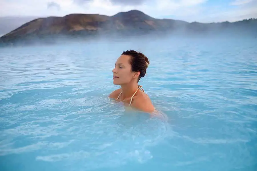 Woman relaxing in the geothermal waters of a spa in Iceland with misty mountains in the background.