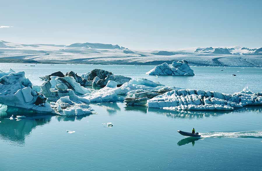 Tourist on a small boat navigating the icy blue waters of Jökulsárlón Glacier Lagoon with floating icebergs, scenic mountains in the background, Iceland