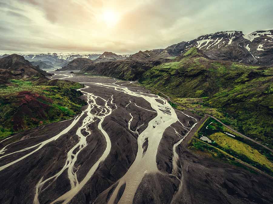 Aerial view of Landmannalaugar in Iceland, showcasing the vividly colored rhyolite mountains and winding glacial rivers under a subdued sunset.