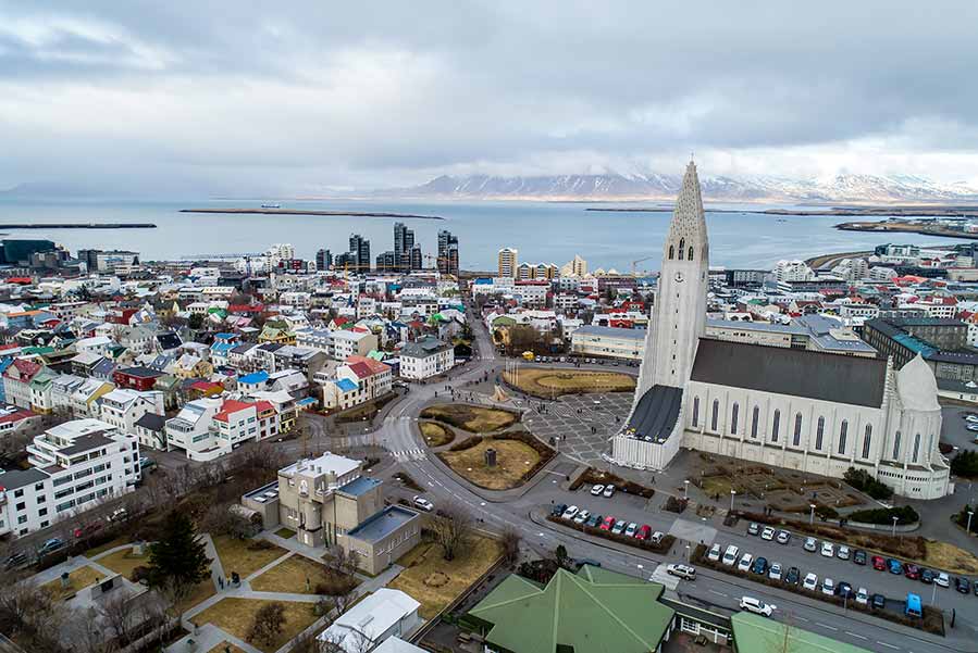 Aerial view of Reykjavik, Iceland showcasing the Hallgrimskirkja church and scenic surroundings with colorful rooftops and the ocean in the background.