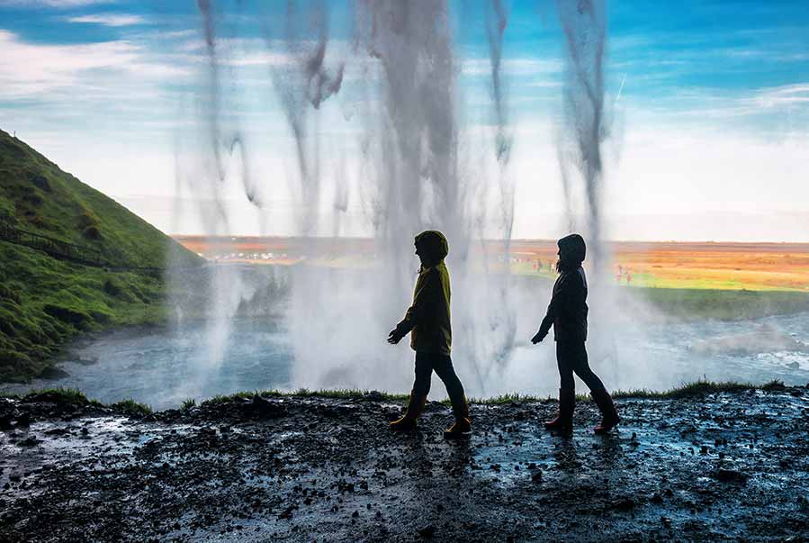 Tourists walking behind the magnificent Seljalandsfoss Waterfall in Iceland, showcasing its breathtaking scenery and cascading waters.