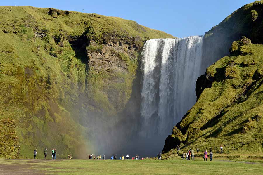 Skogafoss waterfall in Iceland, a popular tourist spot with visitors admiring the majestic cascade and vibrant green surroundings on a sunny day.