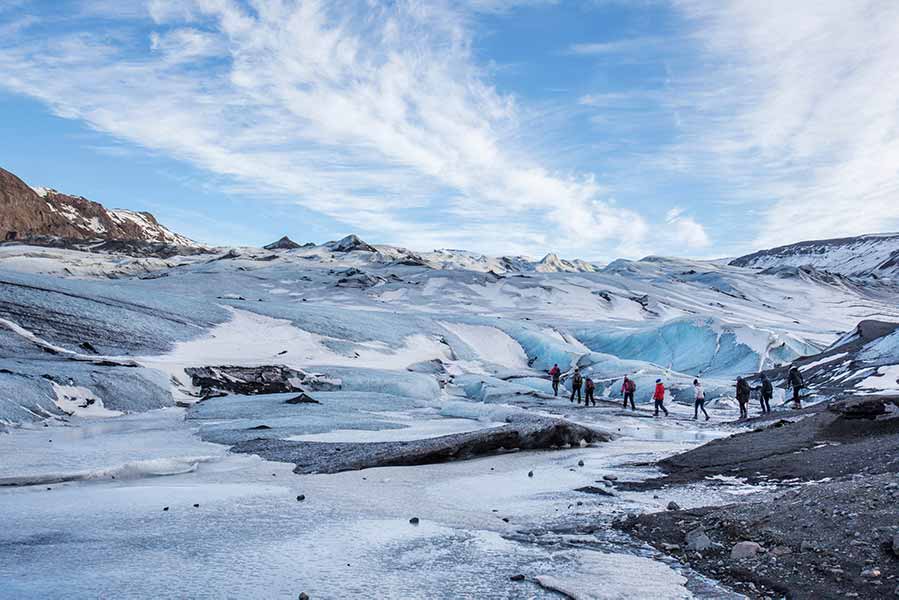 Tourists exploring the icy terrain of Sólheimajökull Glacier in Iceland, showcasing its vast blue ice formations and snowy landscapes.