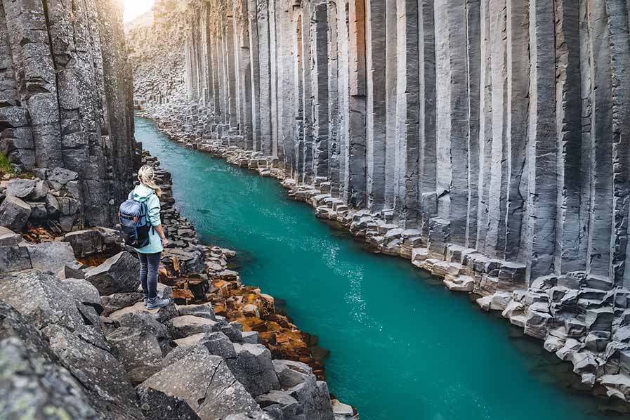 Tourist admiring the stunning basalt columns and vibrant turquoise waters of Studlagil Canyon in Iceland