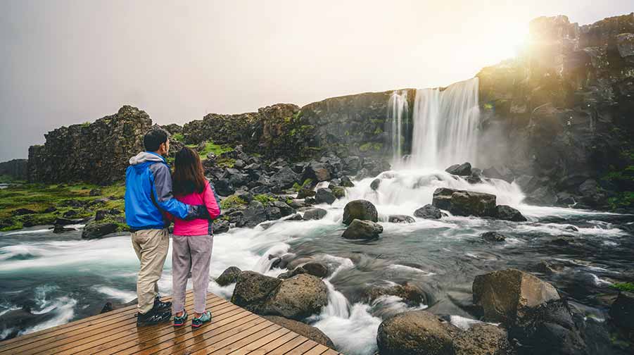 Tourists admiring the stunning waterfall at Thingvellir National Park in Iceland from a wooden viewing platform.
