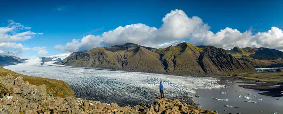 Tourist standing on a cliff overlooking the expansive Vatnajökull Glacier in Iceland, showcasing stunning mountain views and glacial landscapes.