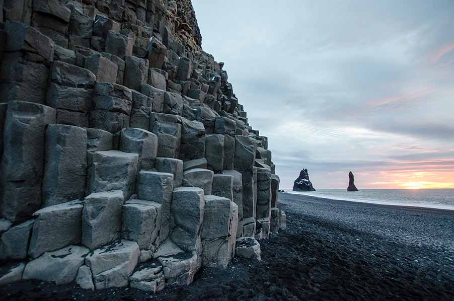 Basalt columns and black sand beach at sunset in Vik, Iceland, highlighting the natural geological formations and rugged coastline typical of Scandinavian landscapes.