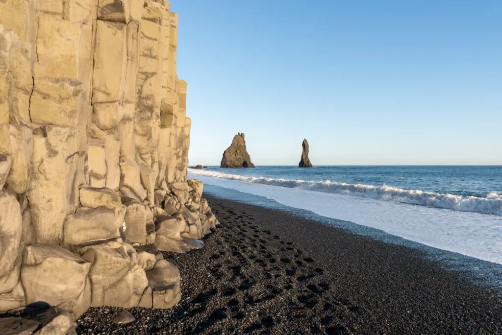 Scenic view of Reynisfjara black sand beach with basalt columns and towering sea stacks under a clear blue sky in Iceland, perfect for nature enthusiasts and photography lovers.