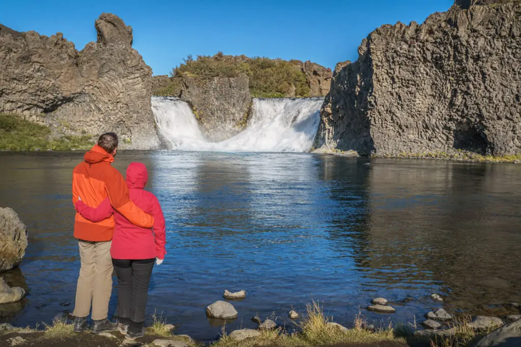 Hiking couple embracing while overlooking the majestic Hjálparfoss Waterfall amidst basalt columns in Þjórsárdalur, Iceland, near Hekla volcano.