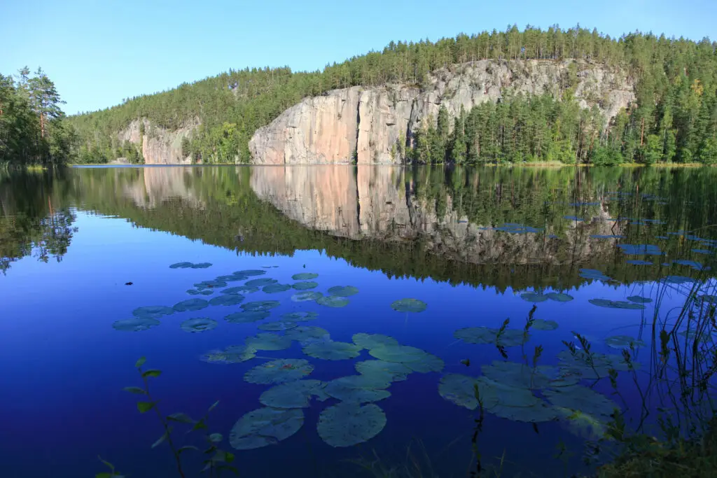 Scenic view of Repovesi National Park in Finland, featuring serene lake waters, lush forests, and towering cliffs reflected perfectly in the calm water.