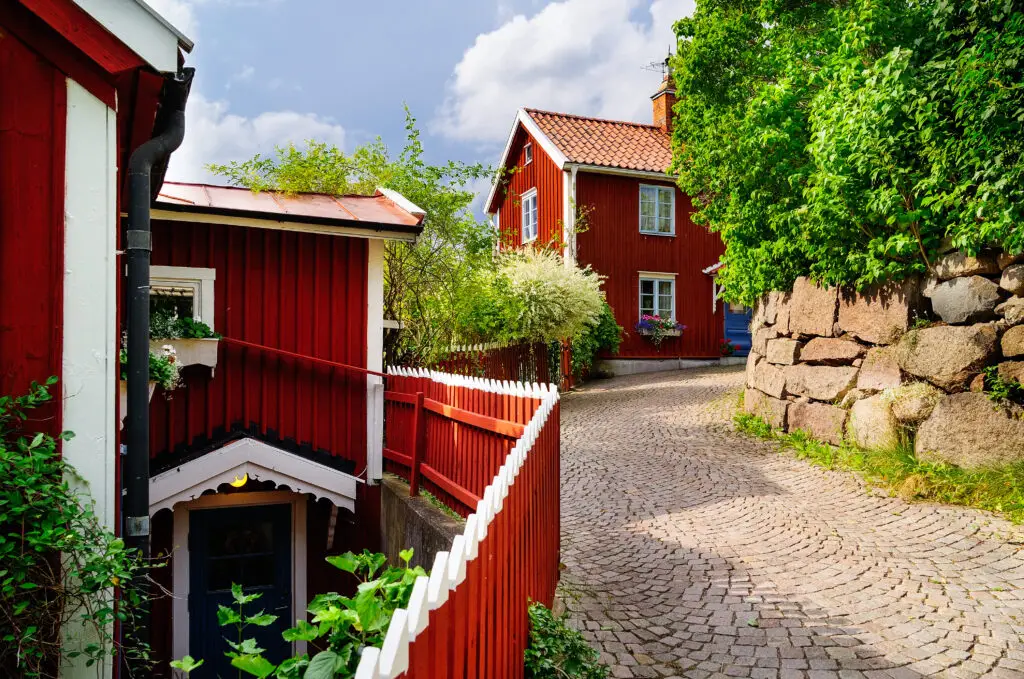 Picturesque view of Batsmansbacken street in Vimmerby, Sweden, famous as the filming location for Astrid Lindgren's Kalle Blomquist, showcasing traditional red Swedish houses and cobblestone streets surrounded by lush greenery.