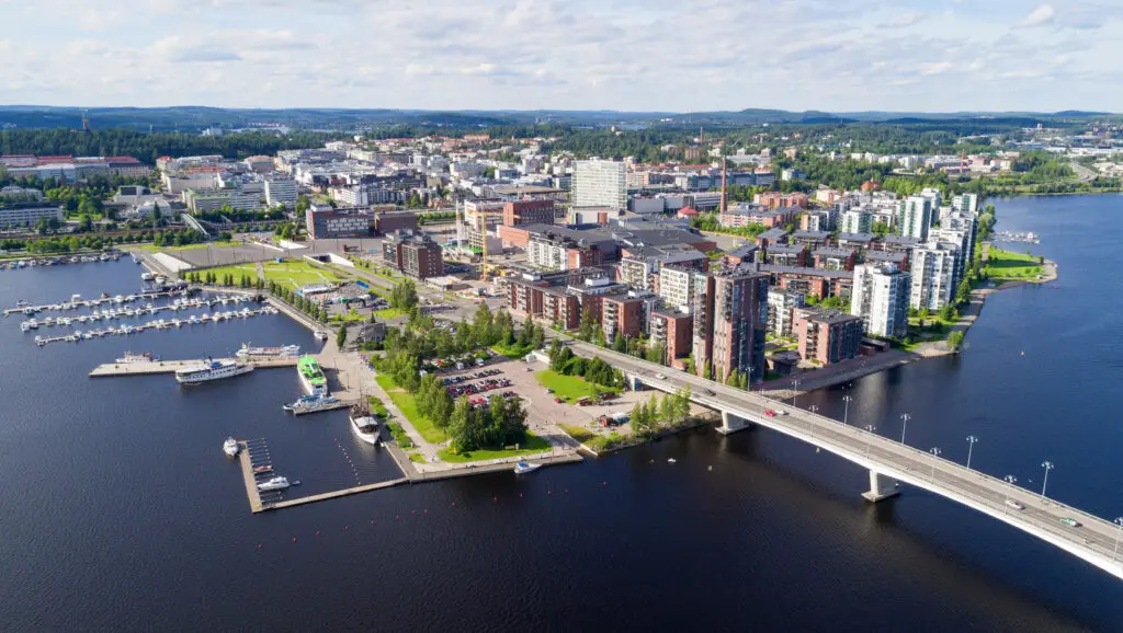 Aerial view of Jyväskylä showcasing the vibrant cityscape with modern buildings, a busy marina, and lush green areas beside a large lake, ideal for promoting tourism in Scandinavia.