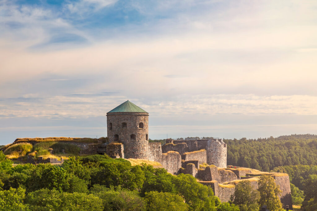 Scenic view of Bohus Fortress ruins on a hillside, surrounded by lush greenery under a soft sky, a popular historical attraction in Scandinavia for tourists.