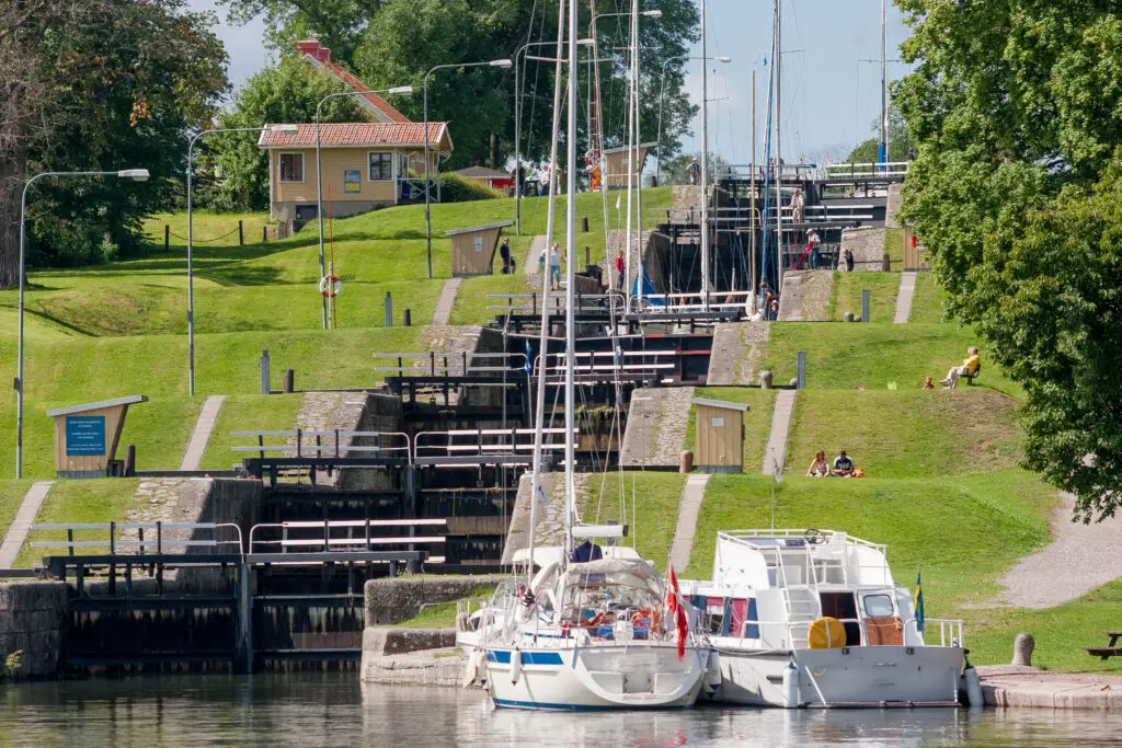 Tour boats docked at the historical Berg Locks on the Göta Canal, Sweden, with tourists and green landscape visible in the background.