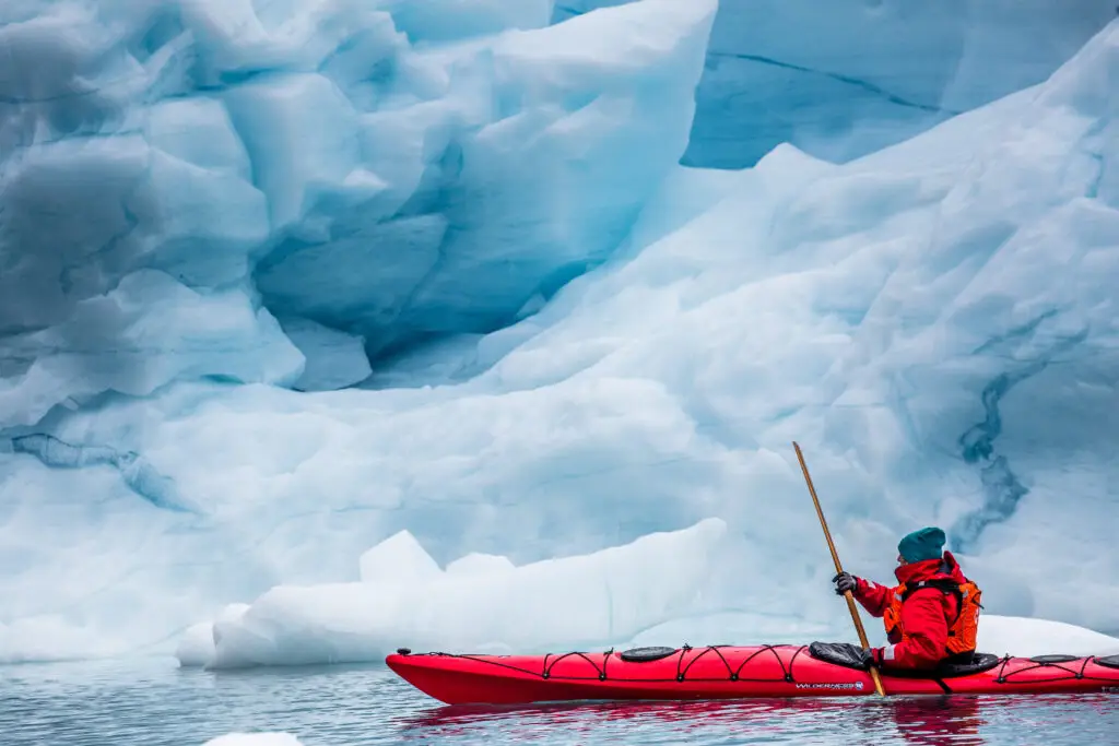 Kayaker navigating through icebergs in Greenland, showcasing the stunning icy landscape and adventure travel opportunities in Scandinavia.