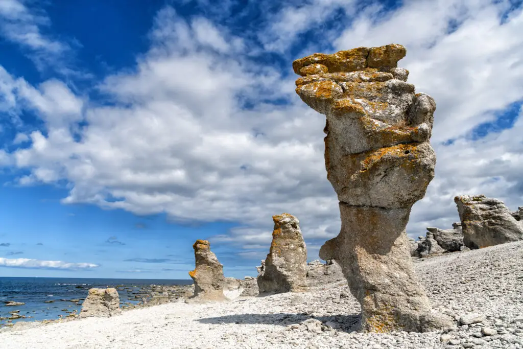 Raukar limestone formations at Gotland, Sweden under a blue sky with fluffy clouds, highlighting natural wonders in Scandinavia for travelers.