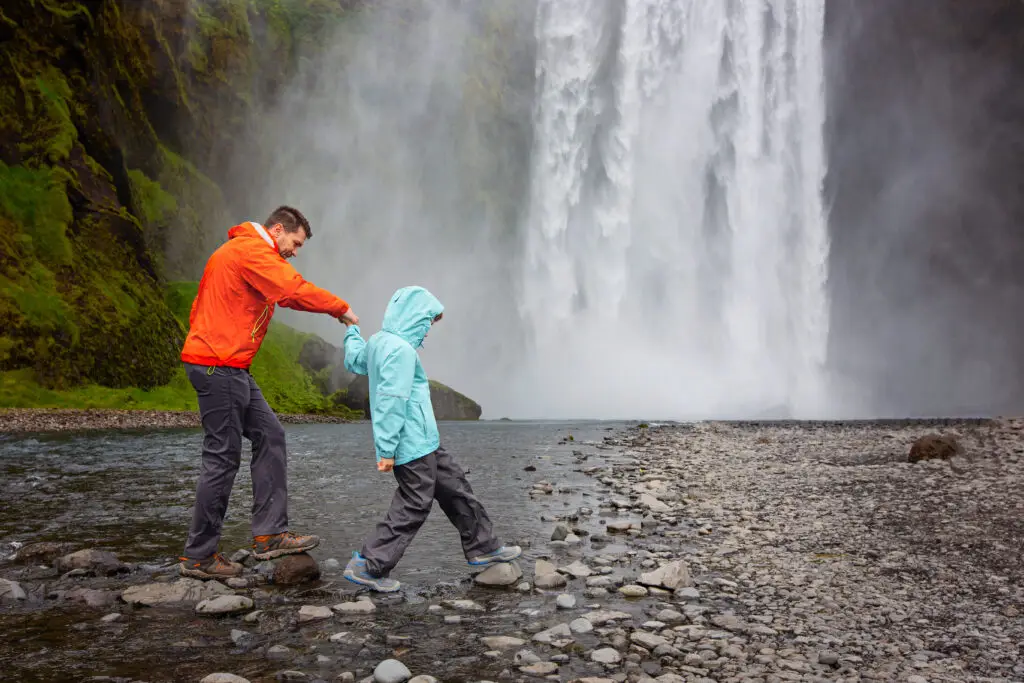 Father and child exploring near a majestic waterfall in Iceland, showcasing a popular tourist attraction in a natural, scenic setting.
