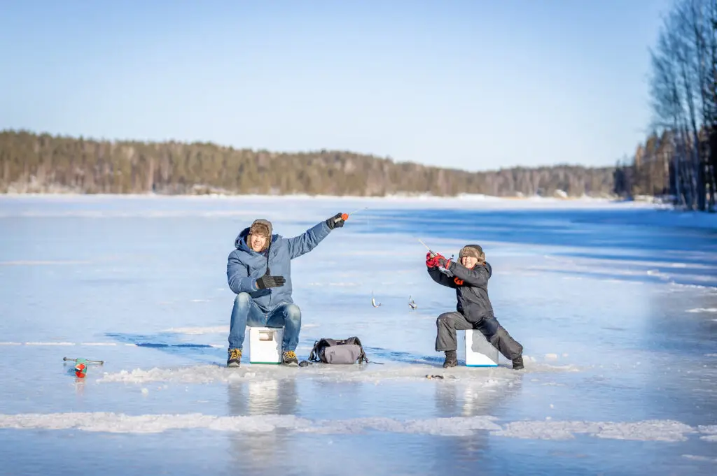 Father and son ice fishing on a frozen lake in Scandinavia, enjoying a sunny winter day outdoors